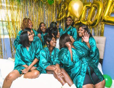 Bridesmaids relax together on a bed wearing matching robes surrounded by balloons before the wedding celebration.